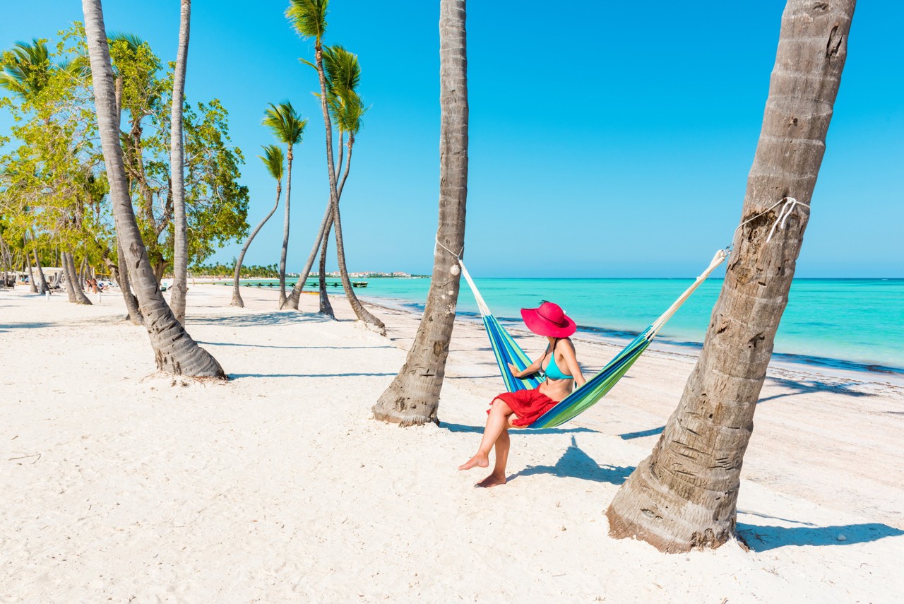 Juanillo Beach (playa Juanillo), Punta Cana, Dominican Republic. Woman relaxing on a hammock on a palm-fringed beach.