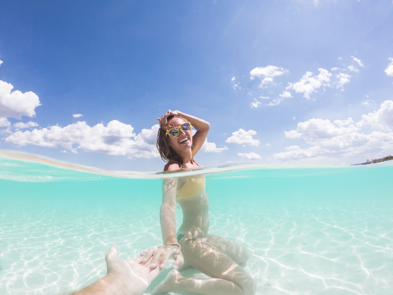 Half split underwater shot view of woman holding man's hand in pristine clear water beach in Mexico