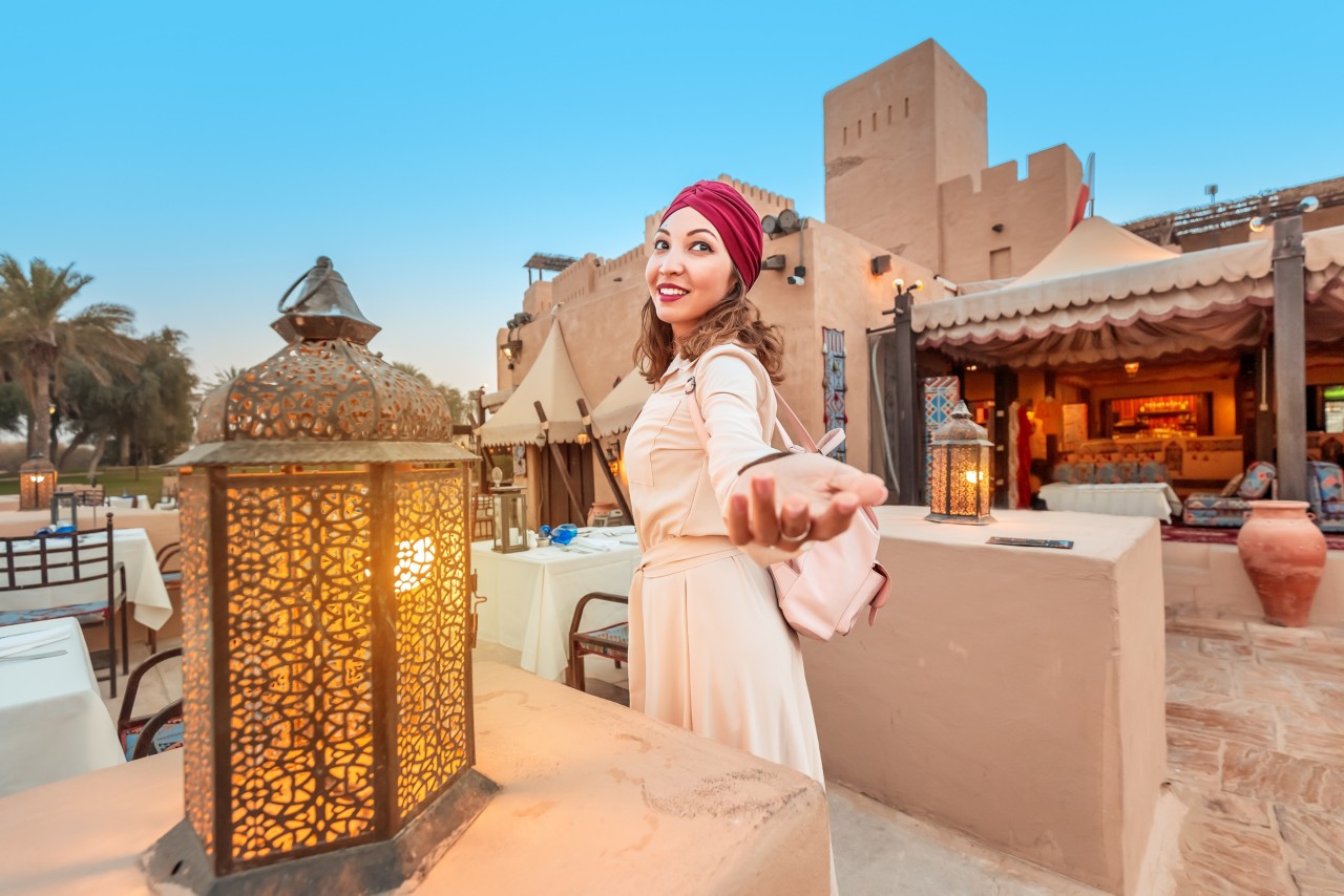 1204032200 Follow happy woman traveler wearing dress and turban walking through the streets of an old Arab town or village in the middle of the desert. Concept of tourism and adventure alone