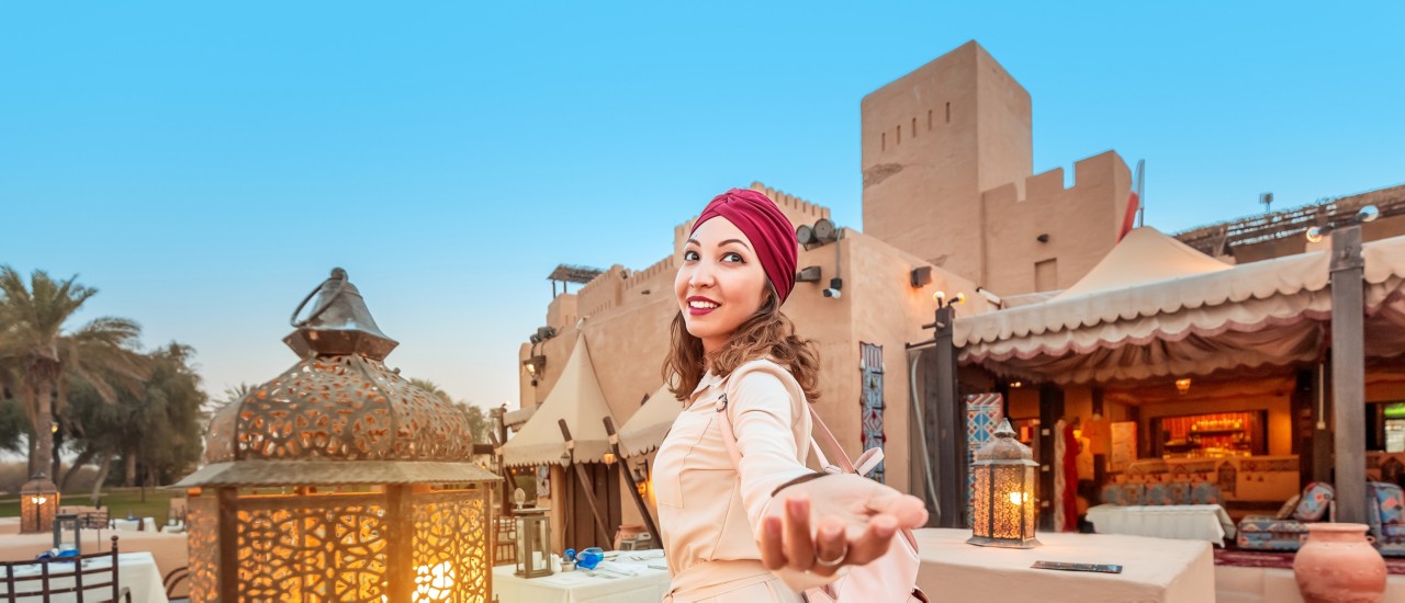 Follow happy woman traveler wearing dress and turban walking through the streets of an old Arab town or village in the middle of the desert. Concept of tourism and adventure alone