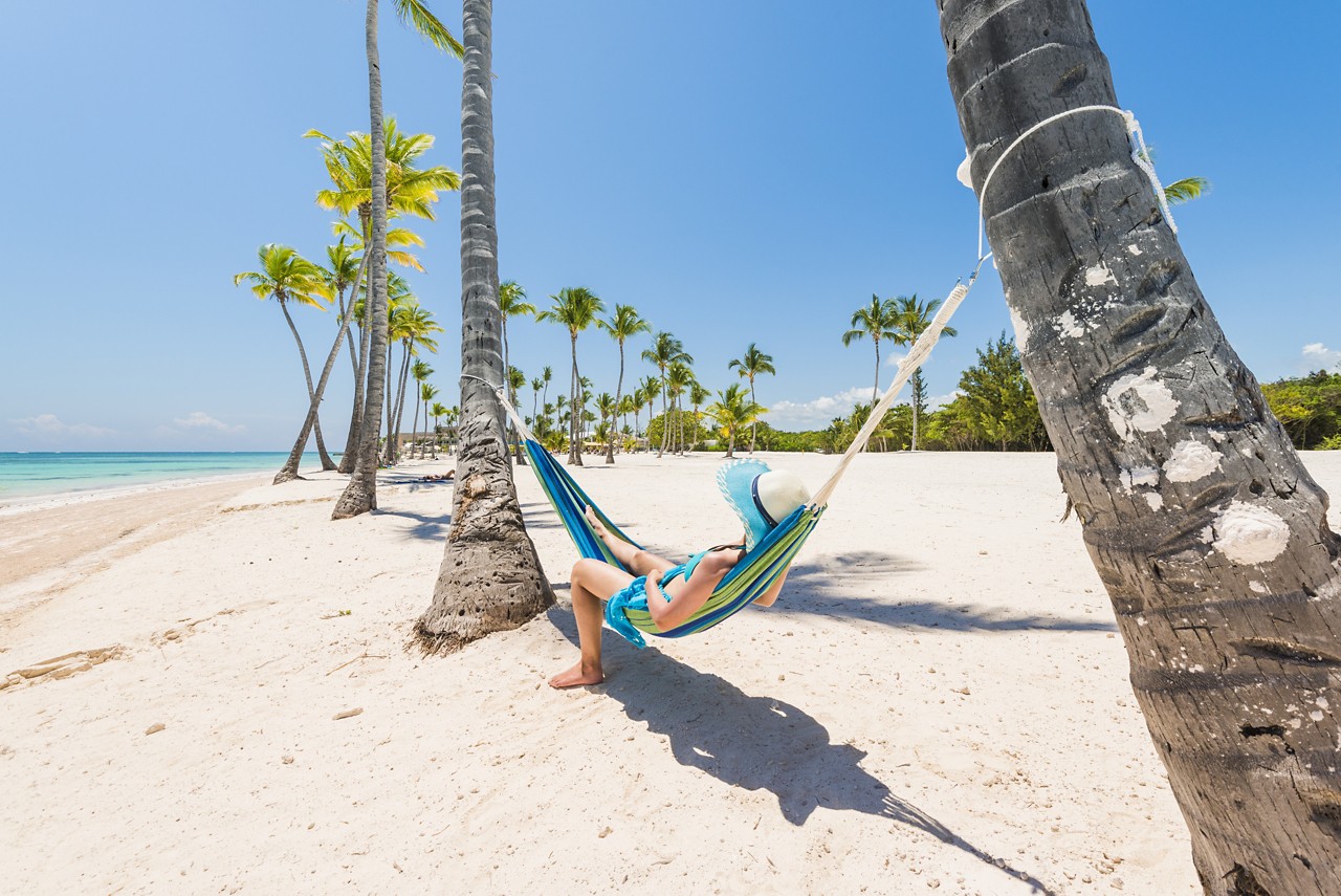 Juanillo Beach (playa Juanillo), Punta Cana, Dominican Republic. Woman relaxing on a hammock on a palm-fringed beach.