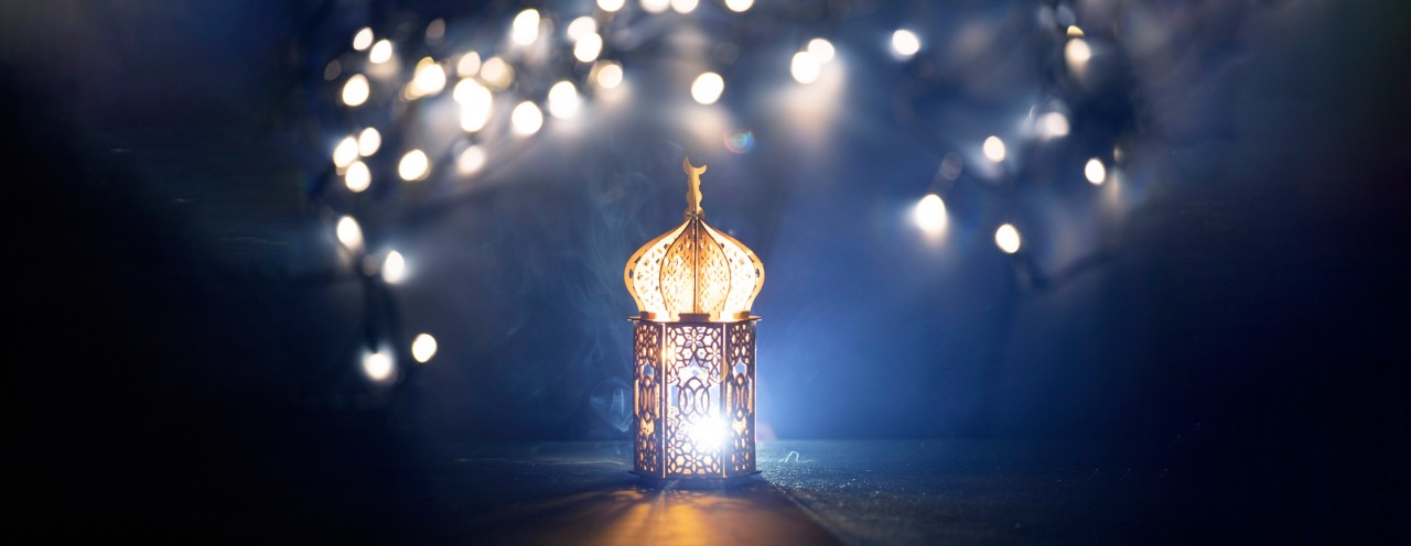 Ornamental Arabic lantern with burning candle glowing at night and glittering golden bokeh lights. Festive greeting card for Muslim holy month Ramadan Kareem.