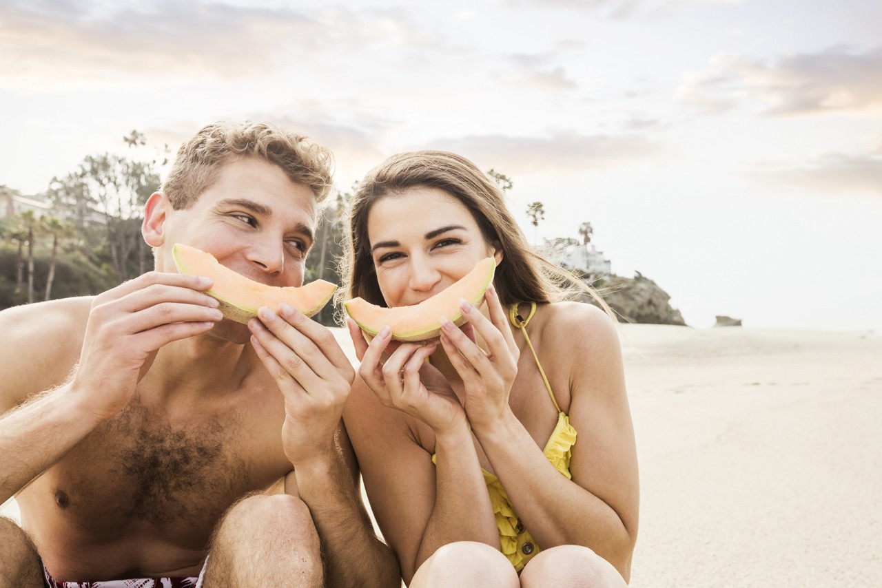 Caucasian couple eating fruit on beach