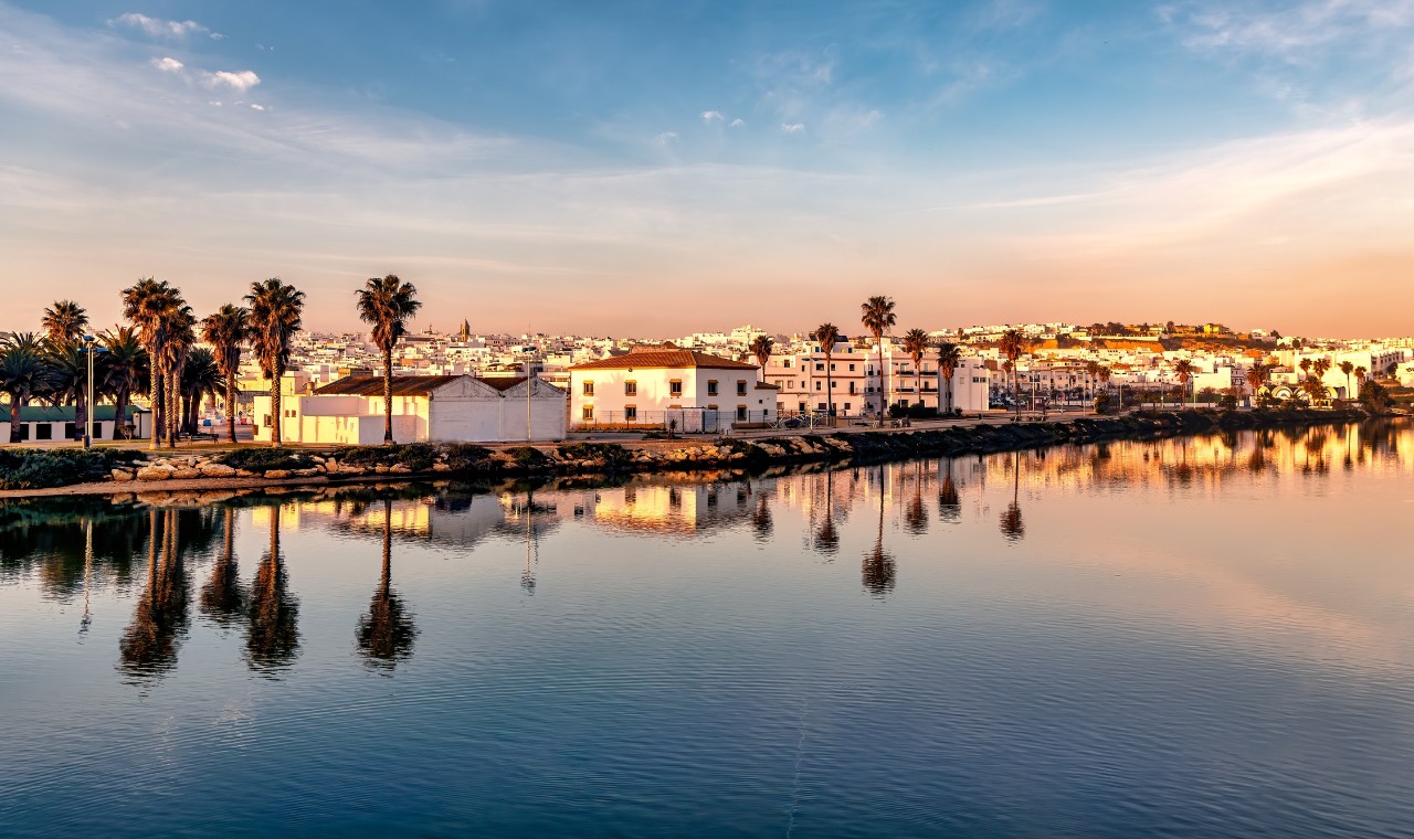 Panoramic view of Conil de la Frontera in southern Spain at sunset, and town reflections on the calm waters of river Salado.