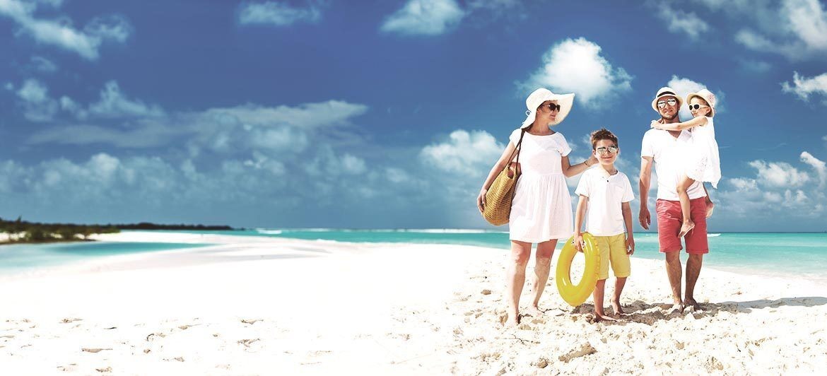 Familienurlaub auf den Balearen: Familie an weißem Strand mit türkisblauem Wasser.