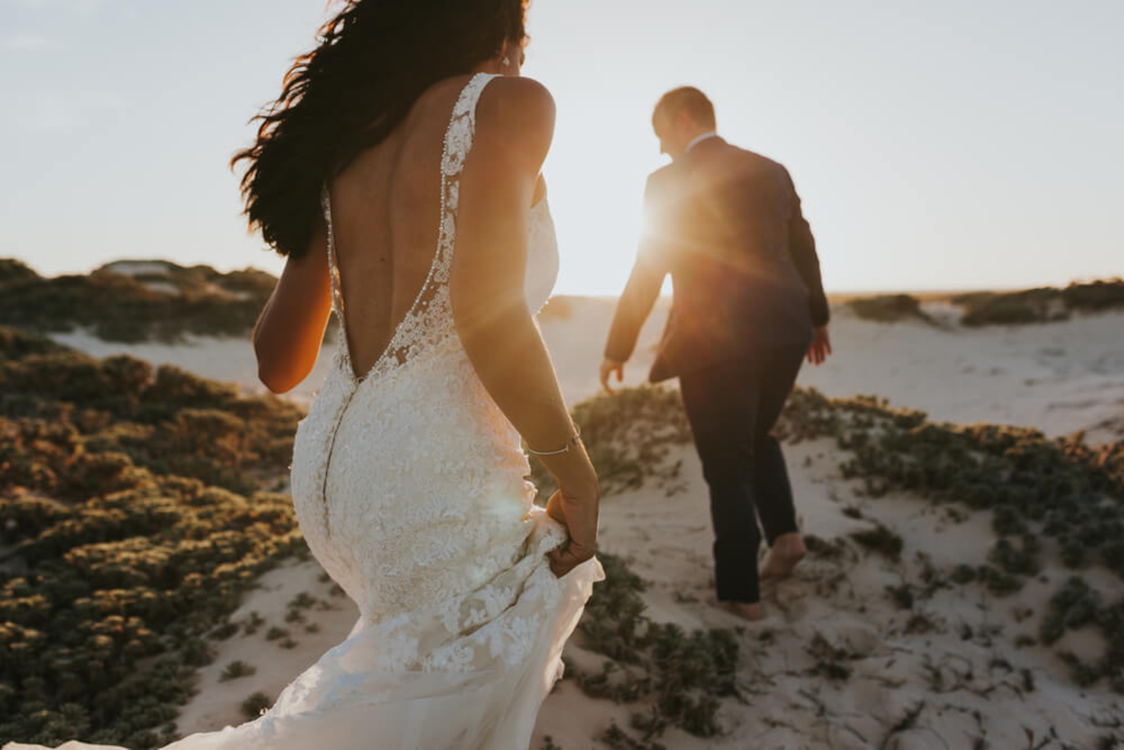 Hochzeit im Freien: Brautpaar geht über Felsen in Strandnähe.
